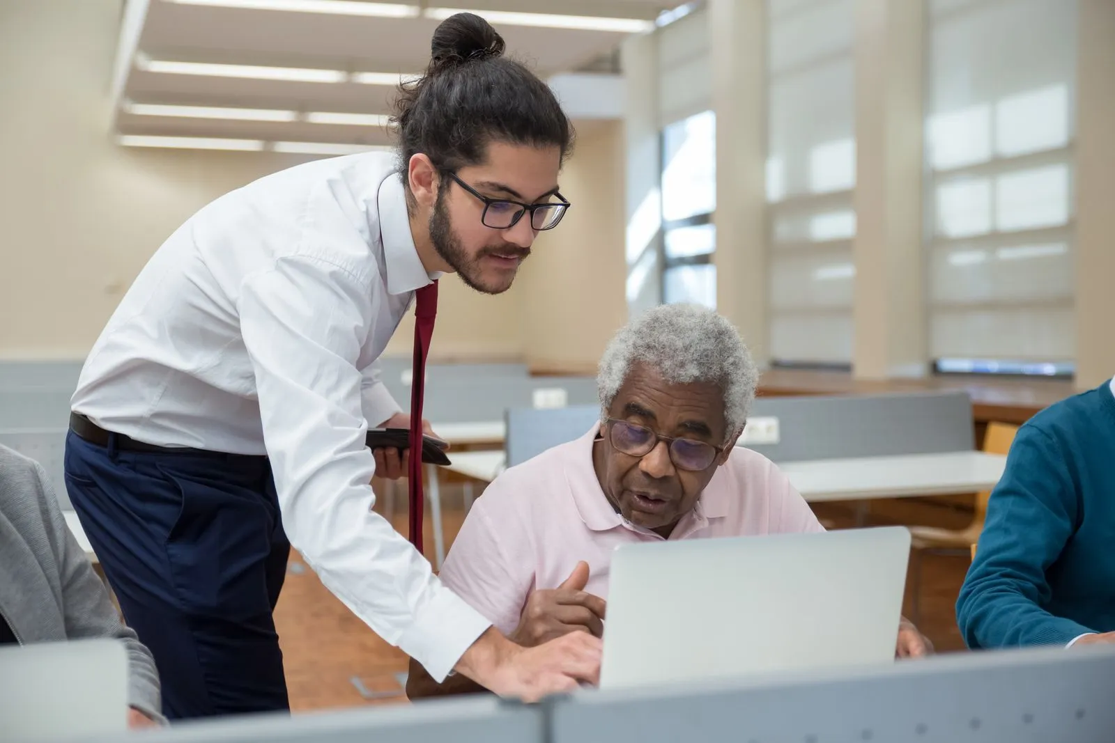 A young instructor helping an older man use a laptop.